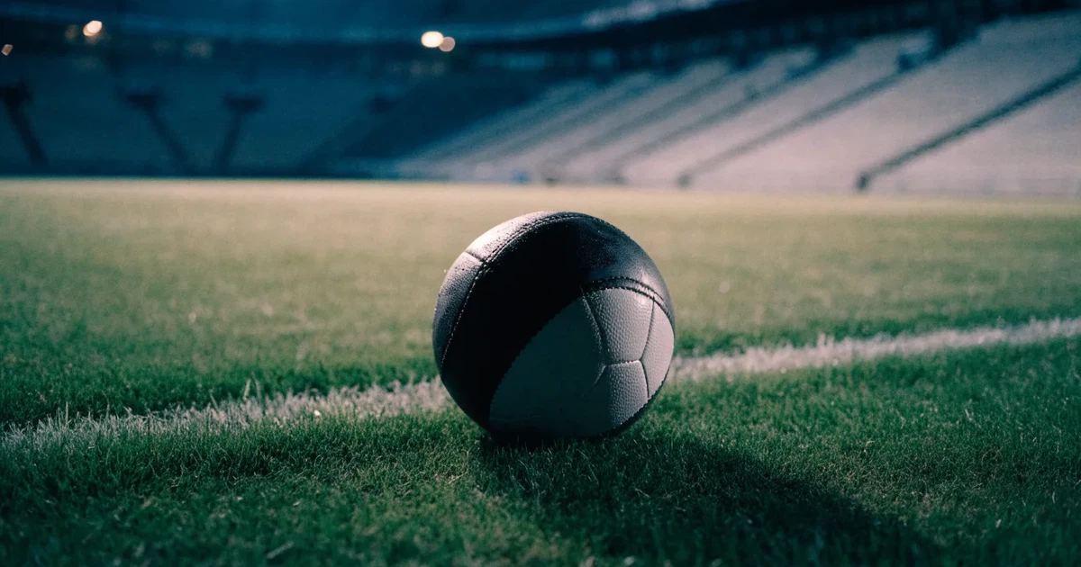 Ein Fußball liegt auf dem Rasen eines leeren Stadions bei Flutlicht, im Hintergrund unscharfe Tribünen ohne erkennbare Beschriftung.