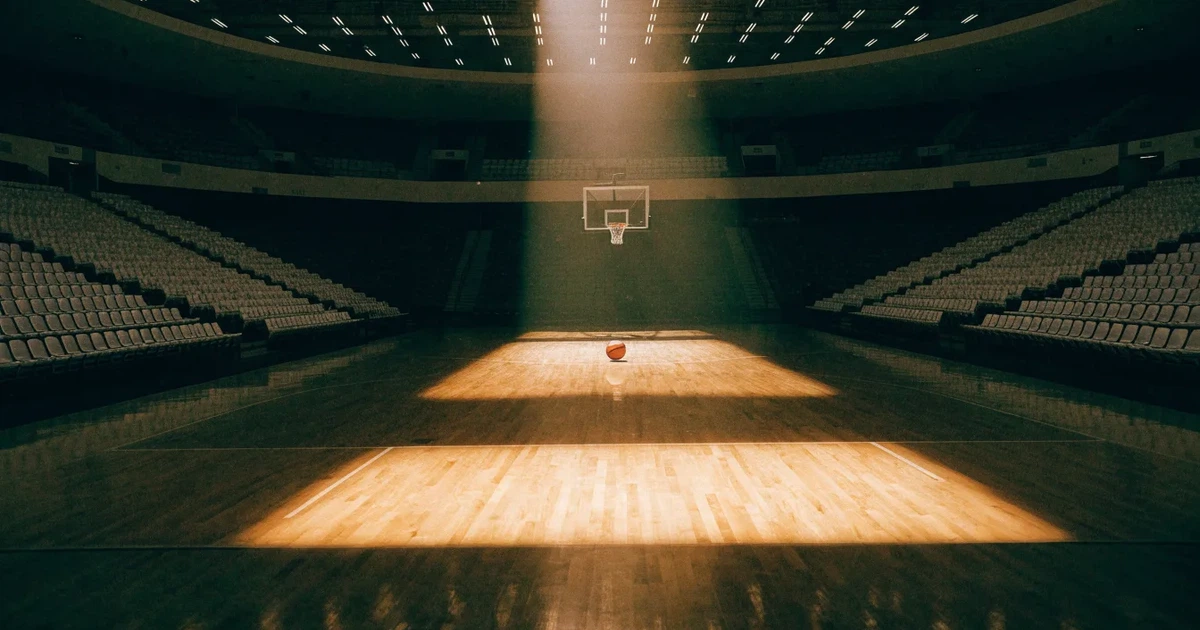 Eine leere Basketballhalle von einer oberen Tribünenreihe aus gesehen, Parkett und Körbe im Licht der Hallenstrahler.