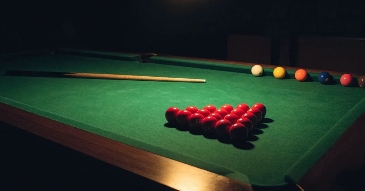 Ein Snookertisch mit grünem Tuch und aufgebauten roten Kugeln in einem abgedunkelten Raum unter einer hängenden Lampe.